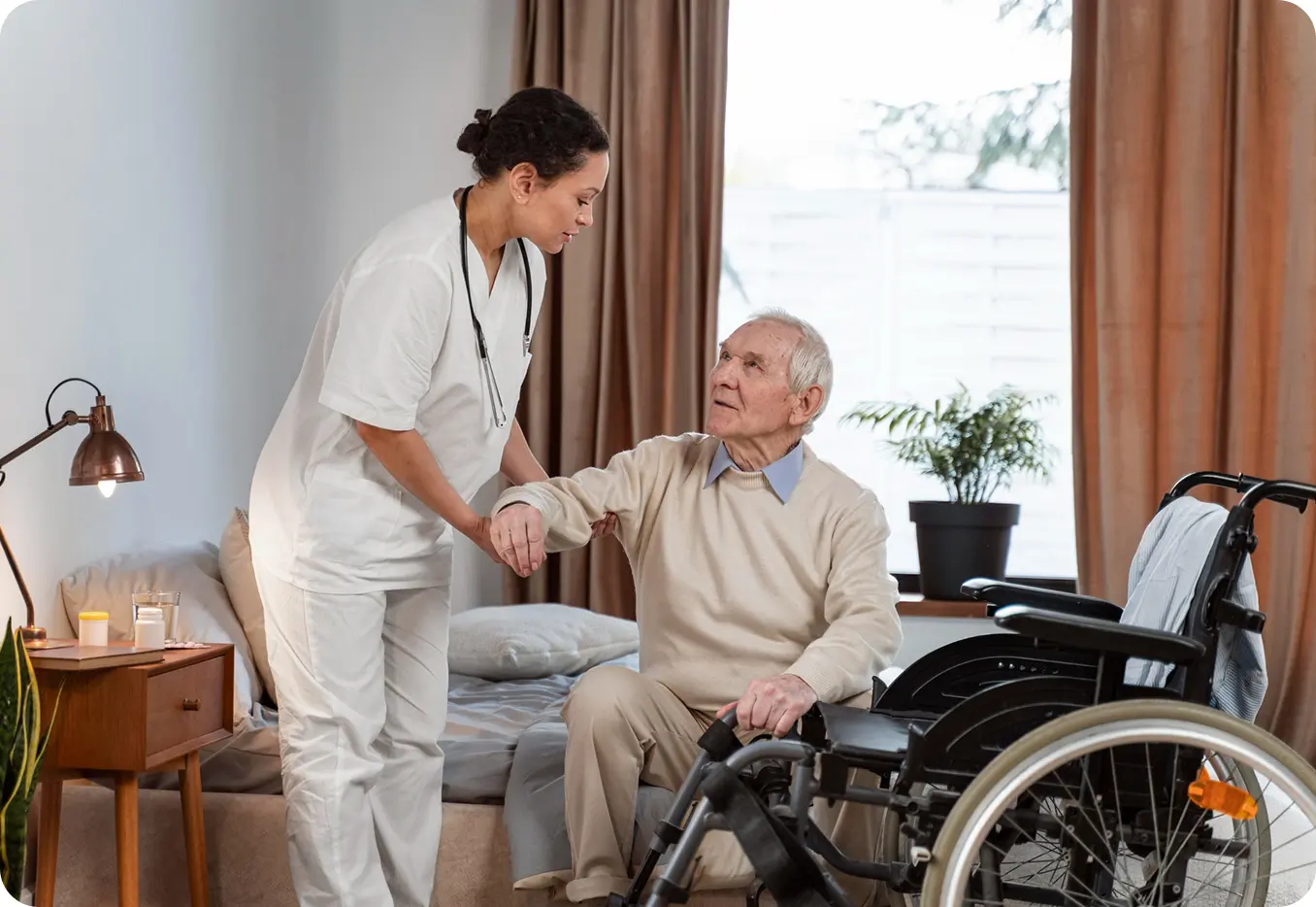 A certified home health aide helping a client move from bed to wheelchair